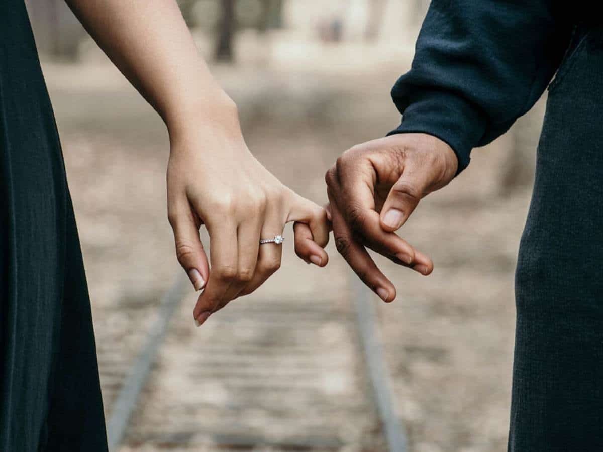 Casal de namorados de mãos dadas e anel dela aparecendo, em sinal de compromisso